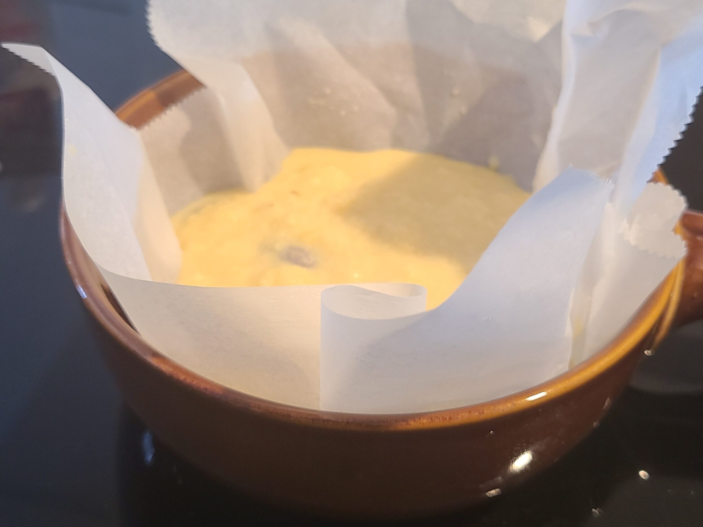茶色い丸いグラタン皿にクッキングシートを敷き、それにパウンドケーキの液が入っている写真。