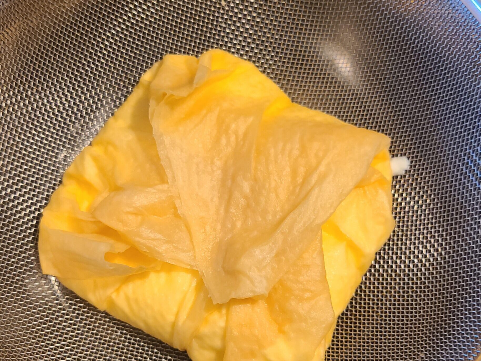 ザルの上でヨーグルトをクッキングペーパーで包んでいる様子。