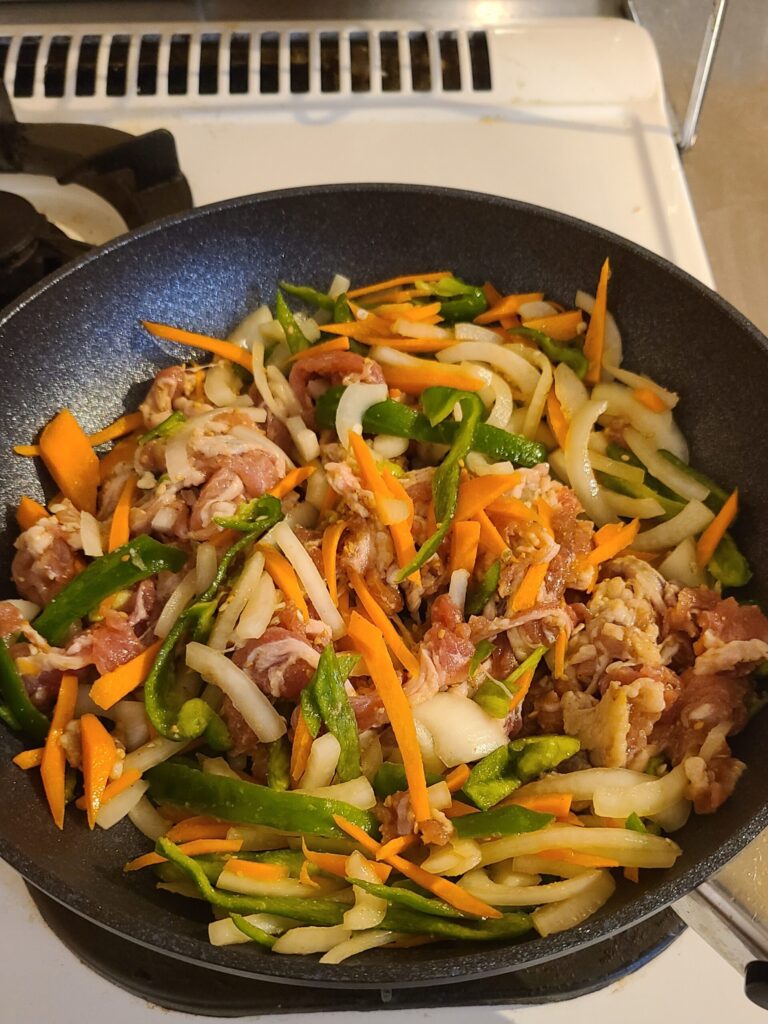 フライパンで焼かれている豚肉と千切りされた野菜