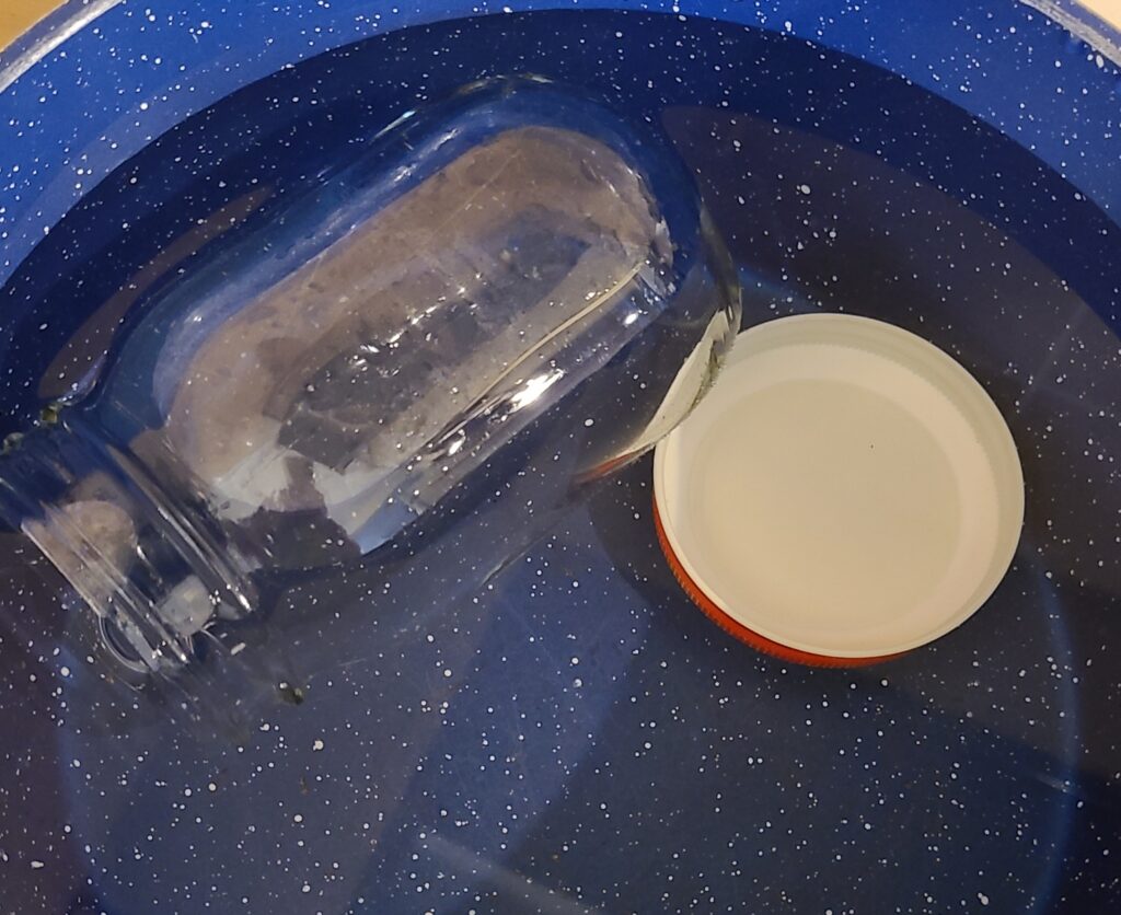 青い鍋の中でガラスの瓶と蓋と水を入れ、煮沸消毒している様子