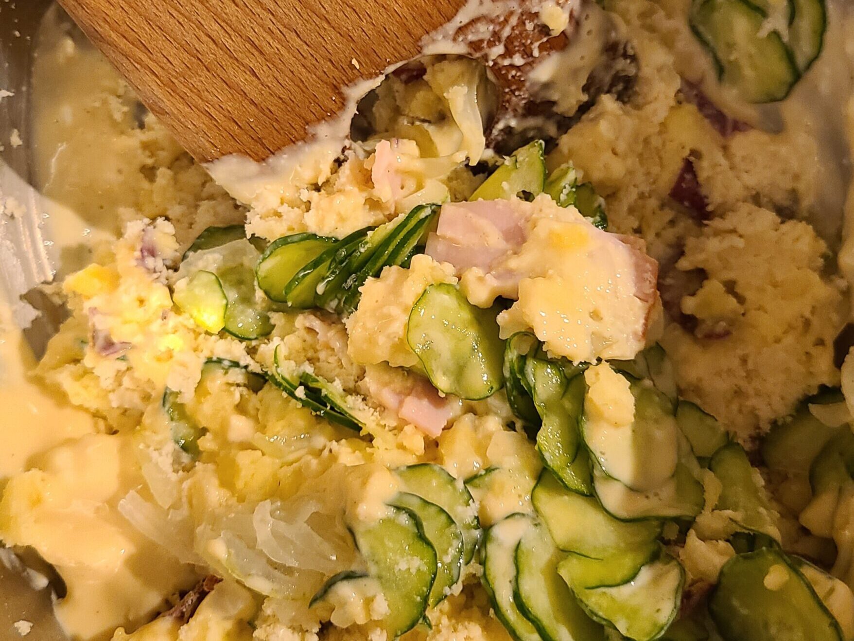 生おからとさつまいものポテトサラダの材料である、スライスされたきゅうりとさつまいもと生おからとはむが木べらで混ぜられている様子。