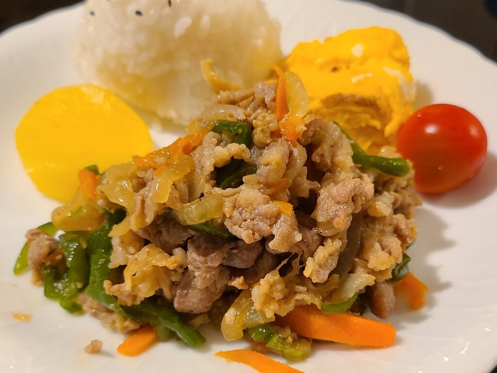 一つのお皿に盛り付けられた豚のプルコギと厚焼き玉子とプチトマトとおにぎりとたくあん