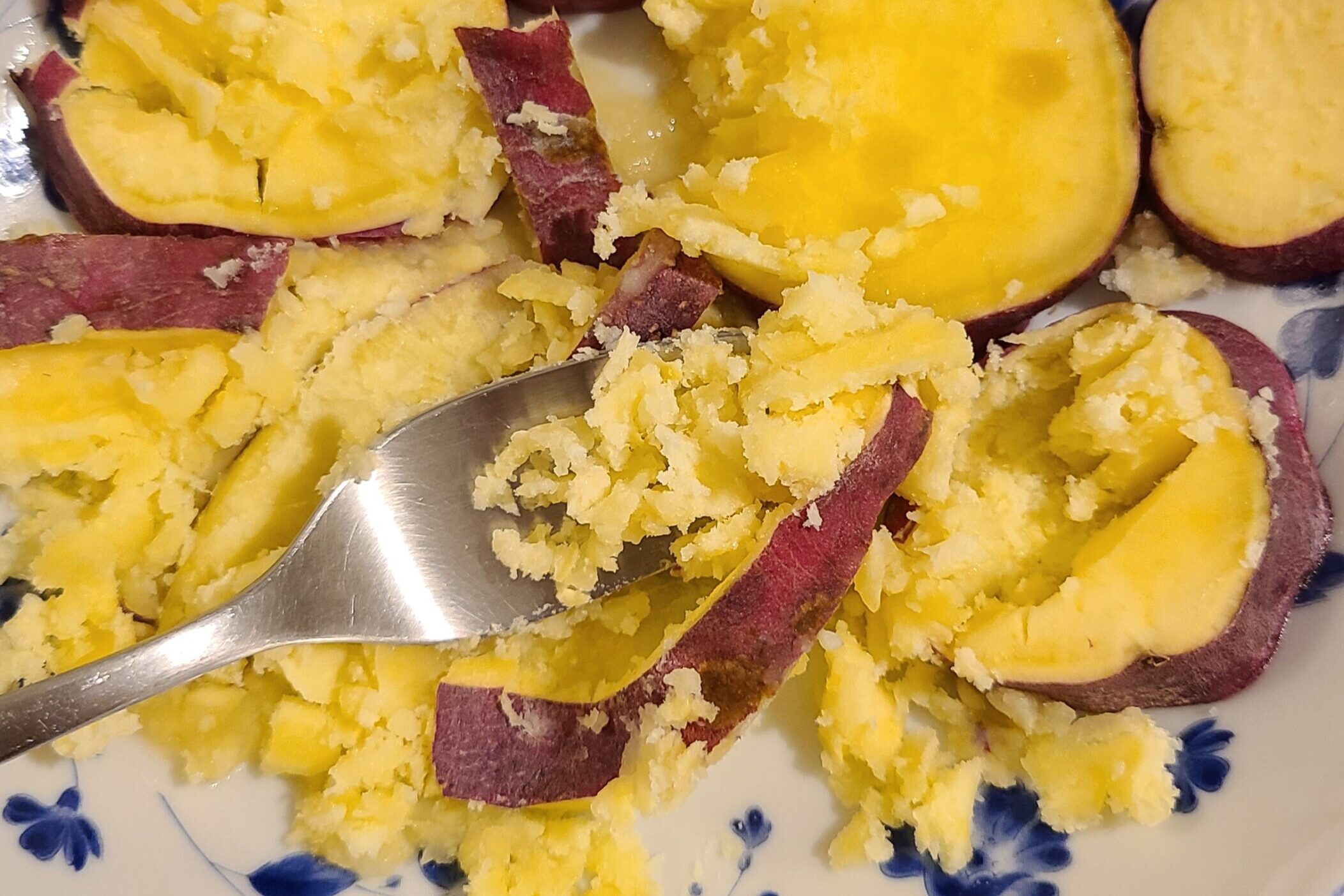 輪切りにされた、レンジで加熱されたさつまいもがフォークの背で潰されている様子。