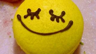 ピンクのお砂糖の上にある、スマイルの顔の黄色いマカロンの写真