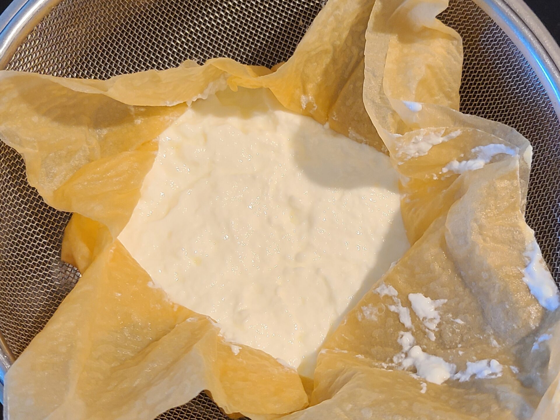 ザルの上にクッキングペーパーを置き、その上にヨーグルトを乗せ水切りをしている様子。