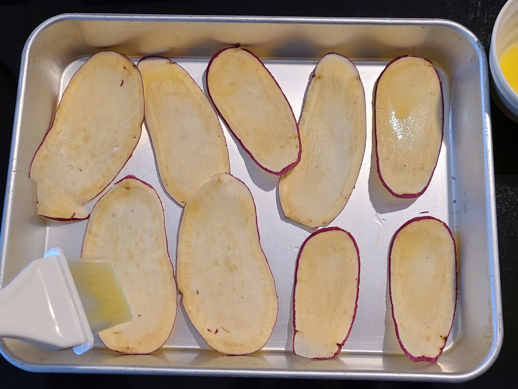 バッドにスライスされたさつまいもを並べ、はけでオリーブオイルを塗っている様子