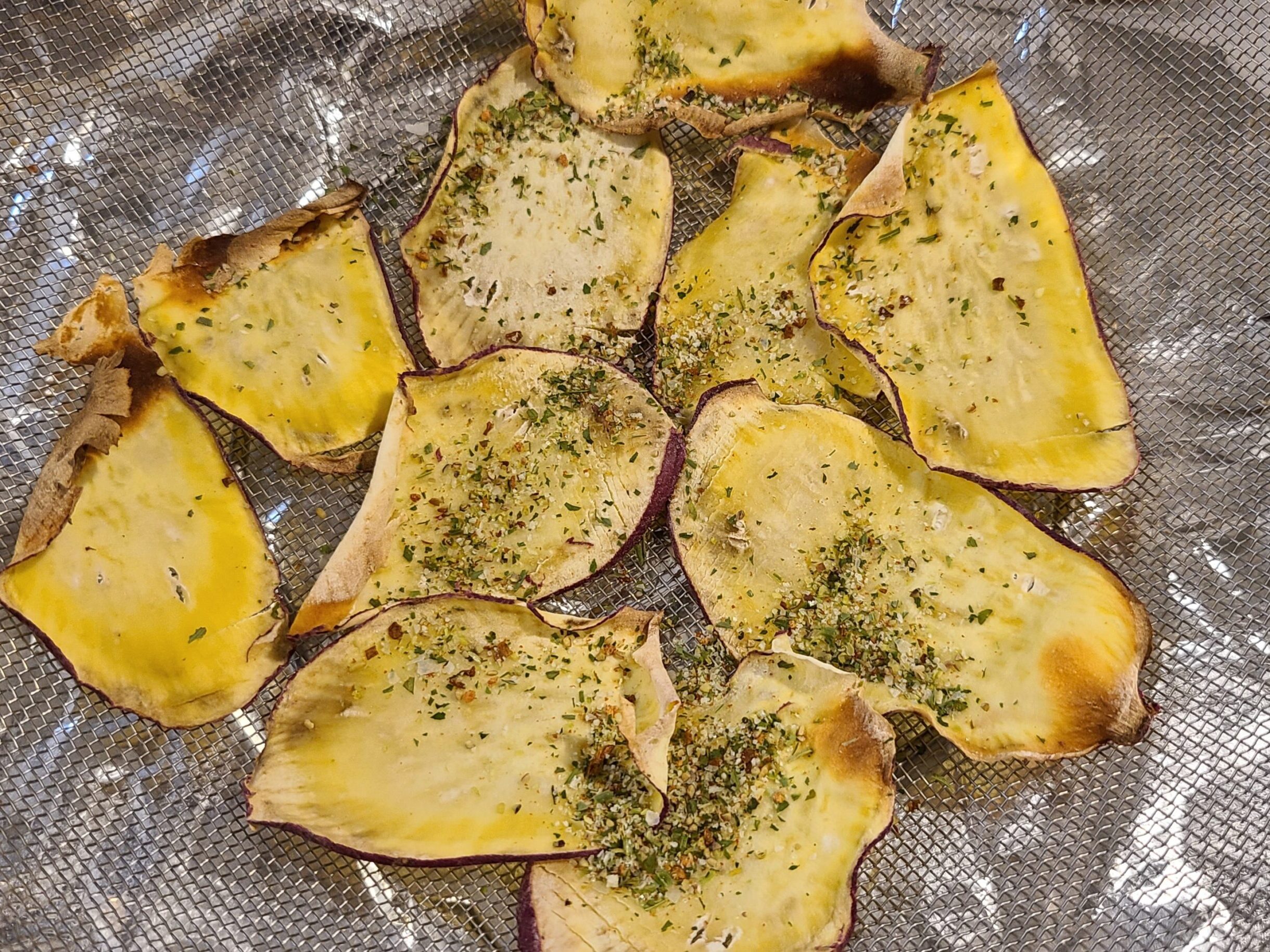 ザルの上にこんがり焼かれたさつまいもチップスを並べ、それらにマジックソルトをかけた写真