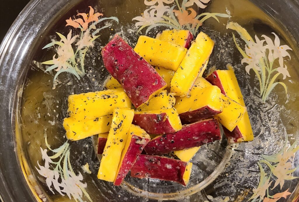 耐熱ボウルの中の味付けされたスティック状のさつまいもに黒ごまがまぶされている様子